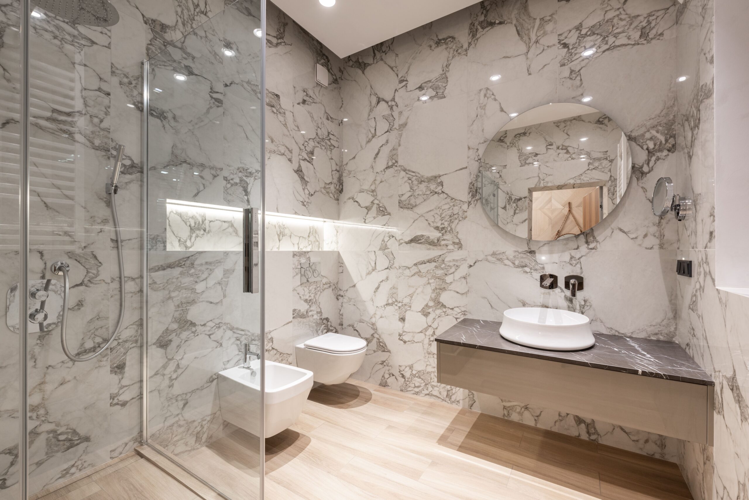 Modern bathroom with marble-look tile walls, glass shower, wall-hung toilet and bidet, and floating vanity with vessel sink